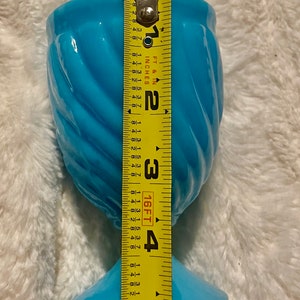 May include: A light blue glass vase with a swirl design and a wide base. The vase is 5 inches tall.
