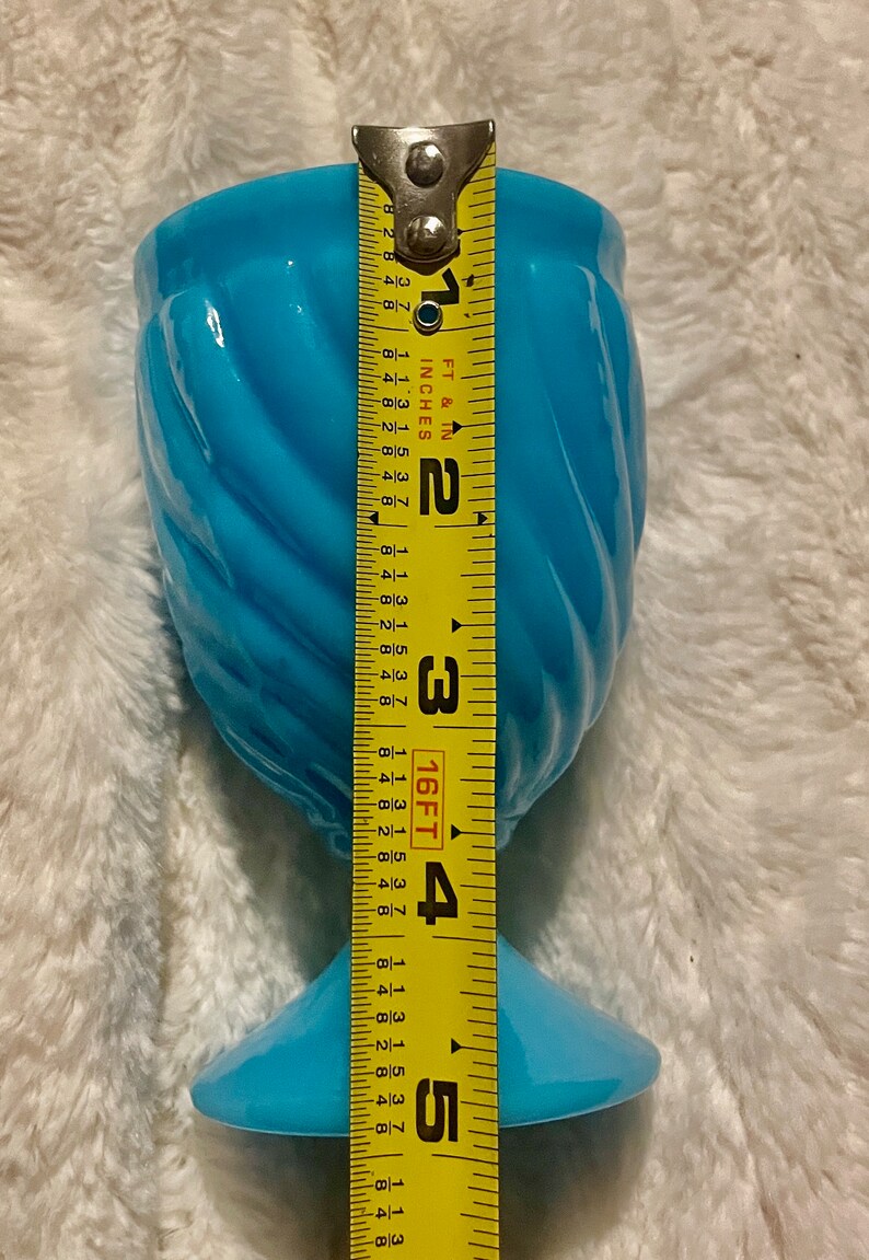 May include: A light blue glass vase with a swirl design and a wide base. The vase is 5 inches tall.