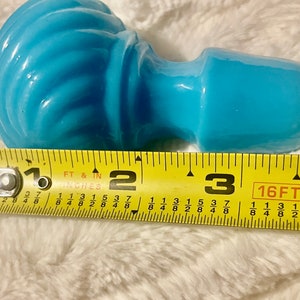May include: A light blue glass bottle stopper with a swirl design. The stopper is approximately 3 inches long.