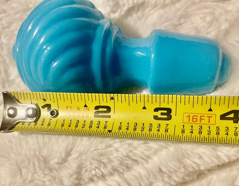 May include: A light blue glass bottle stopper with a swirl design. The stopper is approximately 3 inches long.