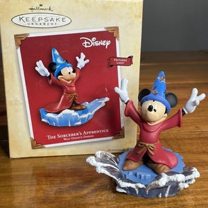 May include: A Hallmark Keepsake Ornament featuring Mickey Mouse as the Sorcerer's Apprentice from Disney's Fantasia. The figurine is in a red robe and blue wizard hat, standing on a blue wave base. The box is visible in the background.