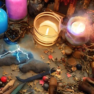 Puede incluir: Una naturaleza muerta con candelabros de vidrio azul, rosa y transparente con velas encendidas. Las velas est&aacute;n rodeadas de varios objetos, incluyendo una roca azul y gris, una rama de madera y hojas secas. La escena est&aacute; iluminada por las velas, creando un ambiente c&aacute;lido y acogedor.
