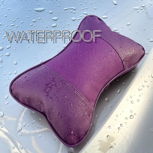 Peut inclure: Un coussin de t&ecirc;ti&egrave;re de voiture violet en forme d'os, avec un design imperm&eacute;able. Le coussin a une surface textur&eacute;e et est recouvert de gouttelettes d'eau. Le mot "WATERPROOF" est affich&eacute; en haut.