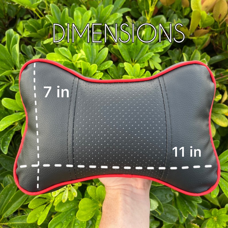 Peut inclure: Coussin de t&ecirc;ti&egrave;re de voiture noir avec garniture rouge, mesurant 28 cm de long et 18 cm de large. Le coussin a une section centrale perfor&eacute;e et le mot "DIMENSIONS" est &eacute;crit en blanc.