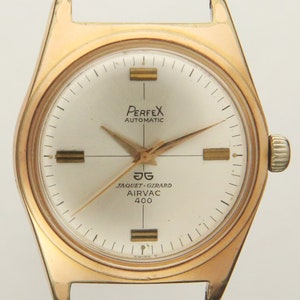 Puede incluir: Un reloj de pulsera de tono dorado con una esfera blanca. La esfera del reloj tiene marcas negras y el texto "PerfeX Automatic", "JAGUET-GIRARD AIRVAC 400" y "SWISS T".