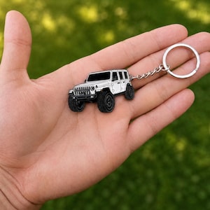 May include: A white off-road vehicle keychain featuring black tires, a black grille, and black windows. The metal charm is attached to a silver-toned circular split ring by a short metal chain, showcasing a detailed miniature SUV design.