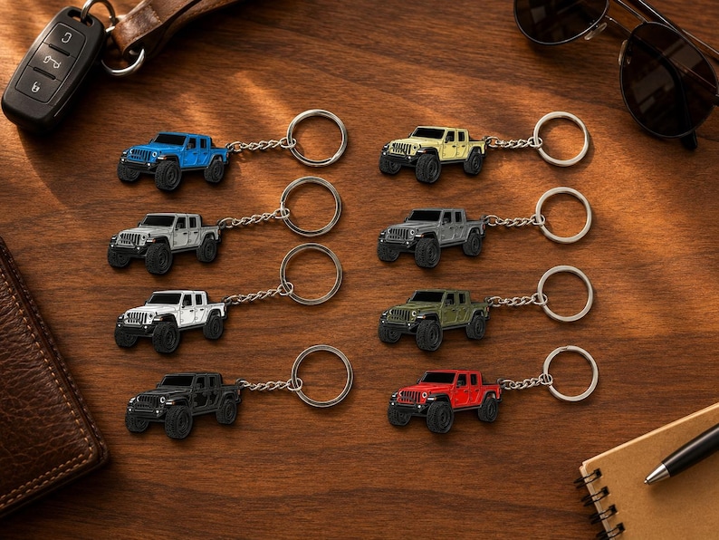 Op de afbeelding: Een verzameling miniatuur Jeep truck sleutelhangers in verschillende kleuren, waaronder blauw, geel, grijs, wit, groen, zwart en rood. Elke sleutelhanger heeft een gedetailleerd truckontwerp met een zilveren sleutelring en ketting. Gerangschikt op een houten oppervlak.