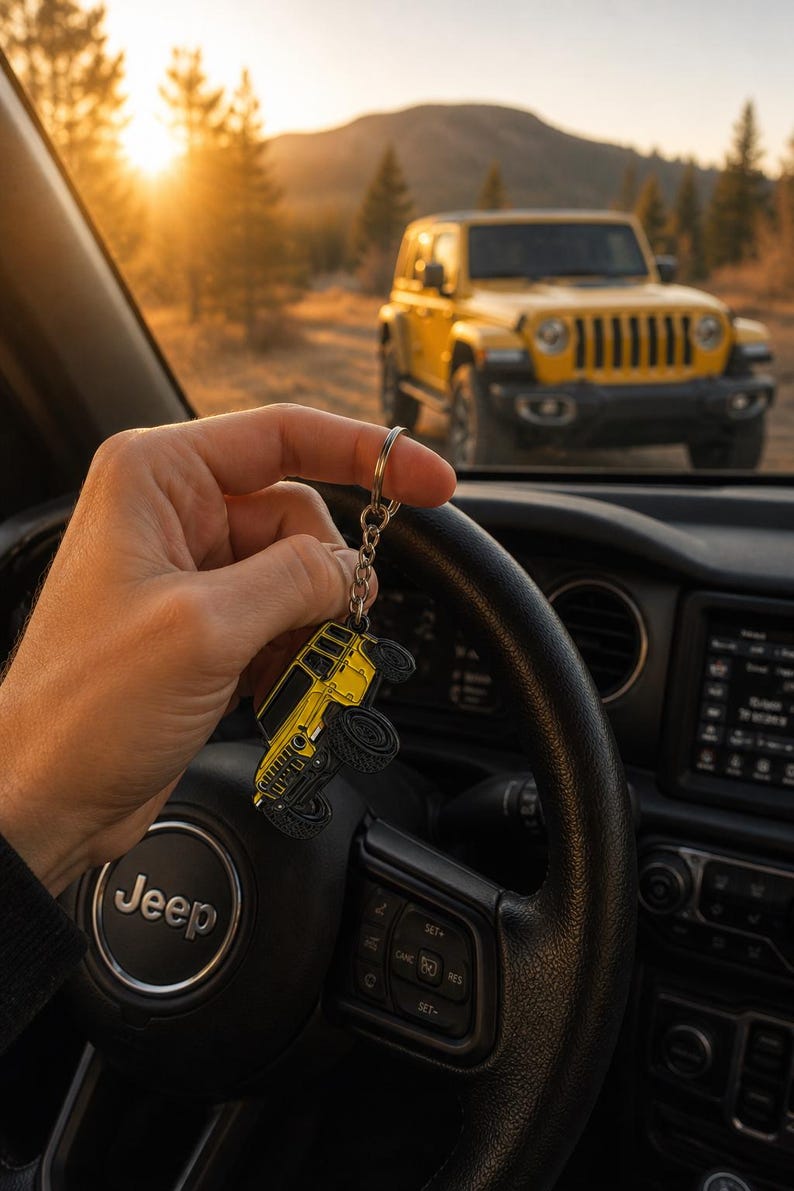May include: A yellow metal keychain shaped like a four-door off-road vehicle with black wheels and detailing, attached to a silver-toned metal split ring and chain, held against the backdrop of a steering wheel and a matching yellow vehicle.
