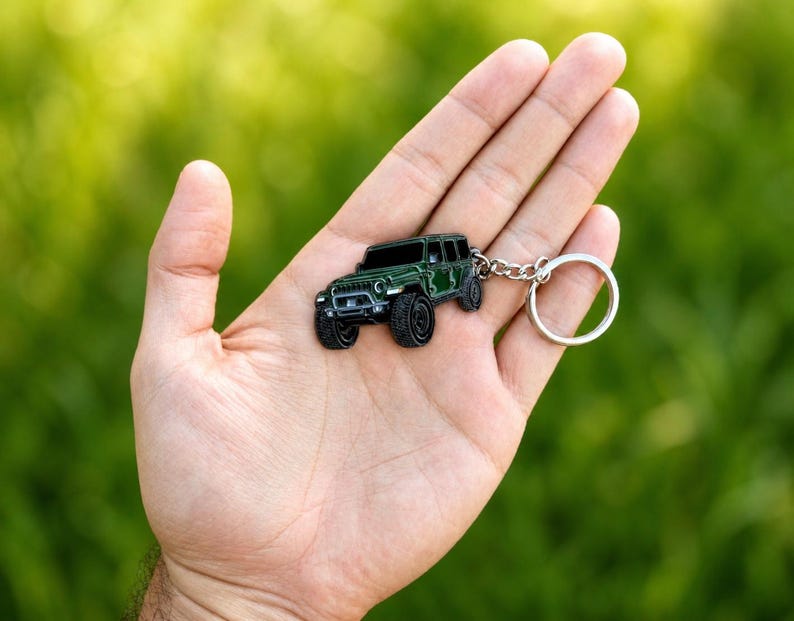 May include: A dark green metal keychain shaped like a four-door off-road vehicle with black tires, a front grille, and a silver-toned circular split ring attached by a short metal chain, showcasing a detailed miniature automotive design.