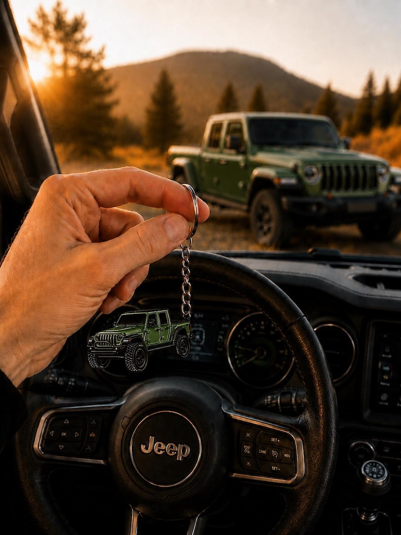 Op de afbeelding: Een groene Jeep-truck sleutelhanger wordt voor een Jeep-stuurwiel gehouden. De sleutelhanger weerspiegelt een groene Jeep-truck die op de achtergrond geparkeerd staat. Het stuurwiel heeft het Jeep-logo.