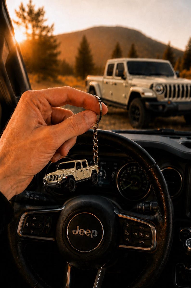 Op de afbeelding: Een sleutelhanger met een beige Jeep pick-up truck bedel. De bedel wordt voor een Jeep stuurwiel gehouden, met een bijpassende Jeep truck op de achtergrond. De sc&egrave;ne speelt zich buiten af met een zonsondergang.