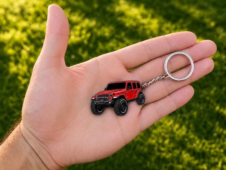 May include: A red off-road vehicle keychain featuring a detailed four-door SUV design with black wheels, a front grille, and a silver metal split ring attached by a short chain, showcasing a realistic miniature representation of a rugged automobile.
