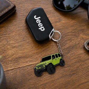 May include: A black Jeep key fob attached to a silver metal keychain featuring a lime green off-road vehicle charm. The charm is a detailed illustration of a four-door SUV with black wheels, black windows, and a front grille design.