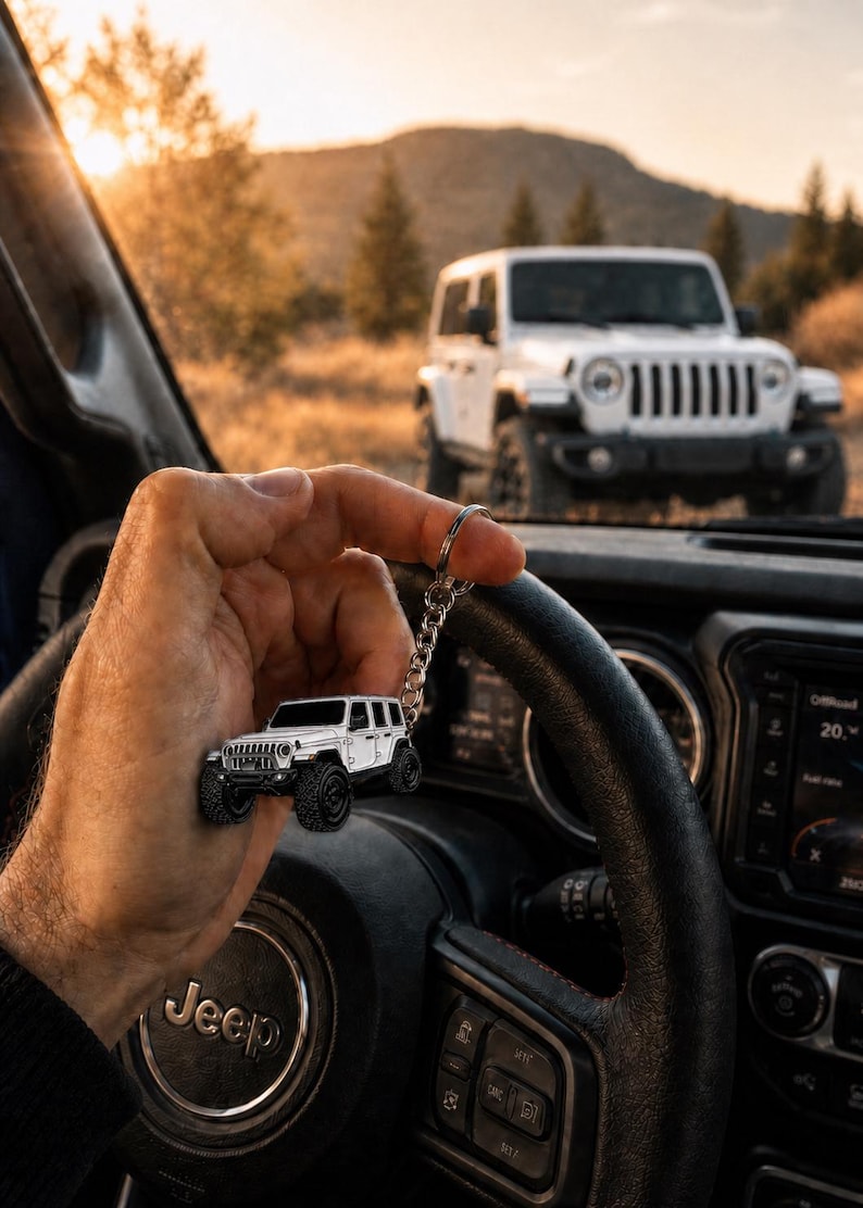 May include: A white off-road vehicle keychain featuring a detailed miniature model of a four-door SUV with black wheels and a silver metal chain ring, held up against the backdrop of a full-sized white SUV parked in a natural outdoor setting.
