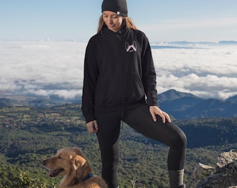 Op de afbeelding: Een zwarte hoodie met een kleine roze afbeelding van hondenoren op de borst, gecombineerd met een zwarte muts, een zwarte legging en wandelschoenen. De hoodie is voorzien van een kangoeroezak aan de voorzijde en lange mouwen.