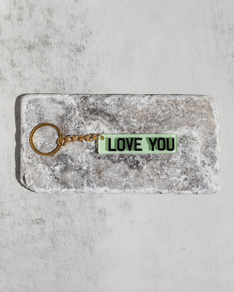 May include: A gold keychain with a green rectangular charm that says "LOVE YOU" in black letters.