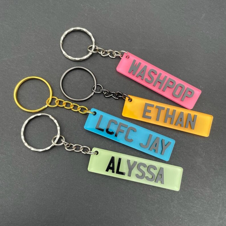 Op de afbeelding: Vier kleurrijke acryl sleutelhangers met zwarte letters. De tags lezen "Washpop", "Ethan", "LCFC Jay" en "Alyssa".