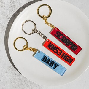 May include: Three keychains with different colored rectangular tags. The tags have black text that reads "SCORPIO", "WM53HGN", and "BABY".