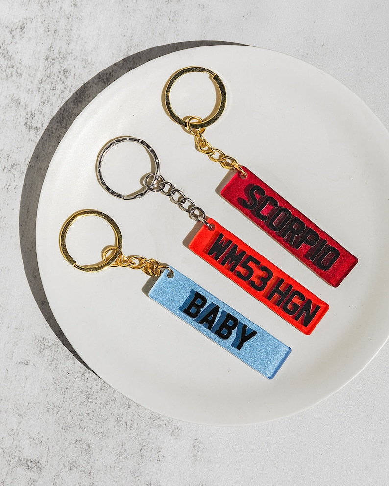 May include: Three keychains with different colored rectangular tags. The tags have black text that reads "SCORPIO", "WM53HGN", and "BABY".
