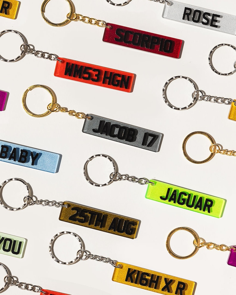 May include: A collection of colorful keychains with different text on each tag. The keychains are made of clear acrylic with black text. The text on the tags includes "ROSE", "SCORPIO", "WM53 HGN", "JACOB 17", "BABY", "25TH AUG", "JAGUAR", "KIGH XR", and "YOU".