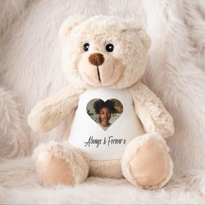 Könnte beinhalten: Ein beiger Teddybär mit einem weißen Shirt, auf dem sich ein herzförmiges Foto eines jungen Mädchens befindet. Das Shirt trägt außerdem den Aufdruck "Always & Forever".
