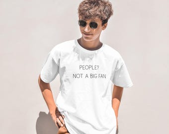 Peut inclure: T-shirt blanc avec le texte "PEOPLE? NOT A BIG FAN" en noir. Le t-shirt est de style col rond. La personne sur l'image porte des lunettes de soleil et un pantalon marron.