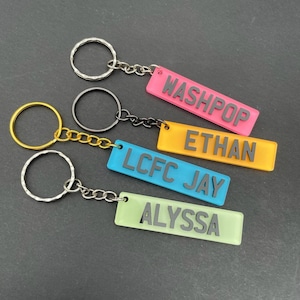 Op de afbeelding: Vier kleurrijke sleutelhangers met verschillende namen. De namen zijn "Washpop", "Ethan", "LCFC Jay" en "Alyssa".