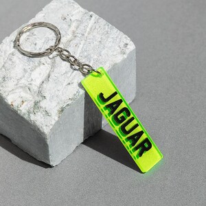 May include: A neon green keychain with a silver key ring and a black rectangular tag that says "JAGUAR" in bold black letters.