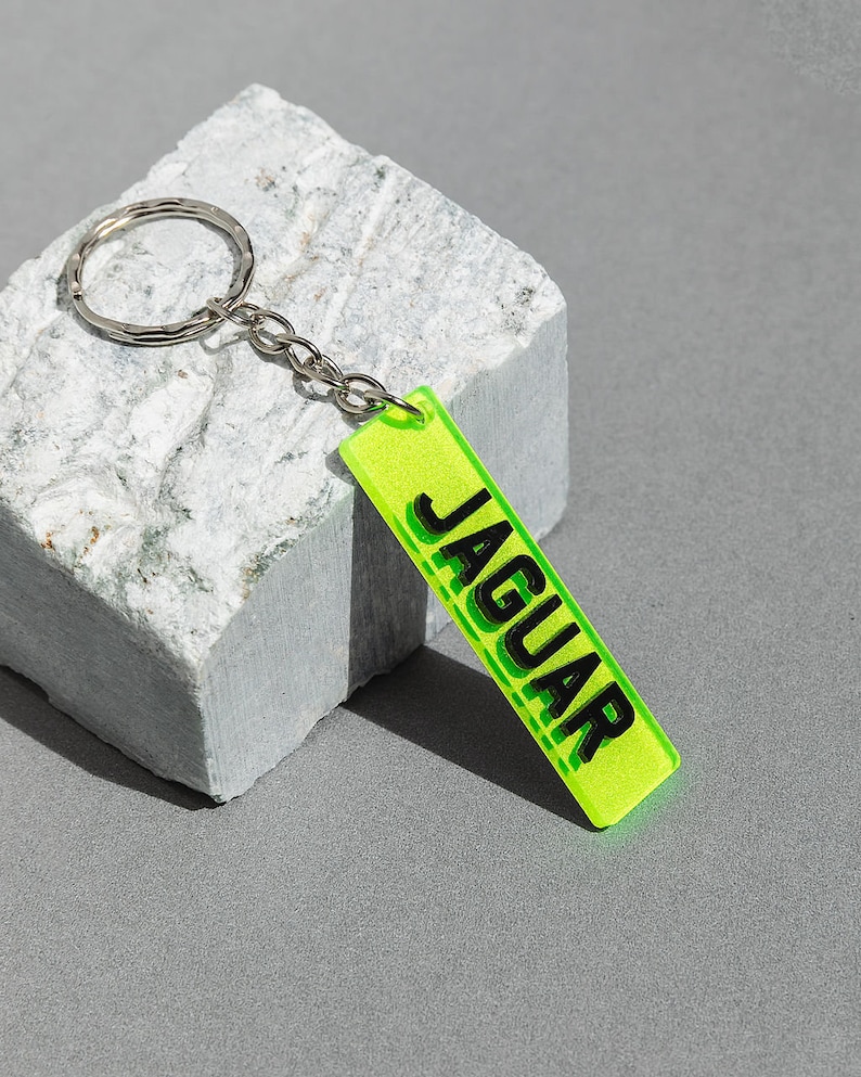 May include: A neon green keychain with a silver key ring and a black rectangular tag that says "JAGUAR" in bold black letters.
