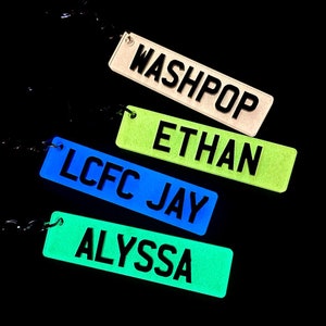 Op de afbeelding: Vijf glow-in-the-dark sleutelhangers met verschillende namen. De namen zijn "Washpop", "Ethan", "LCFC Jay" en "Alyssa".