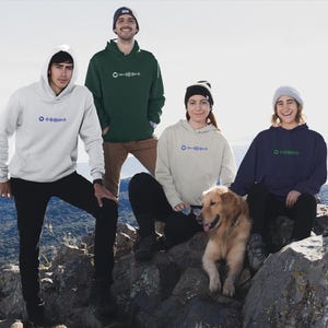 Puede incluir: Cuatro personas con sudaderas con capucha con una nota musical y un patrón de onda en la parte delantera, de pie en la cima de una montaña rocosa con un perro golden retriever. Las sudaderas con capucha son de diferentes colores: verde, blanco, beige y azul marino.