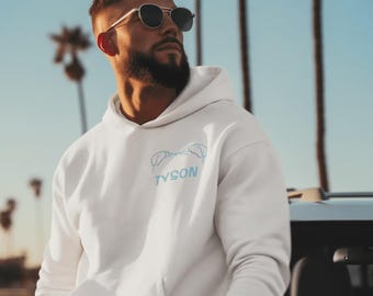 Op de afbeelding: Een wit sweatshirt met lange mouwen en capuchon, voorzien van een lichtblauwe grafische omtrek van een hondenkop en het woord TYSON in het lichtblauw op de linkerborst. De hoodie heeft een kangoeroezak aan de voorzijde en geribde boorden.