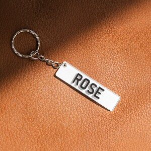 May include: A silver keychain with a white rectangular tag that says "ROSE" in black letters.