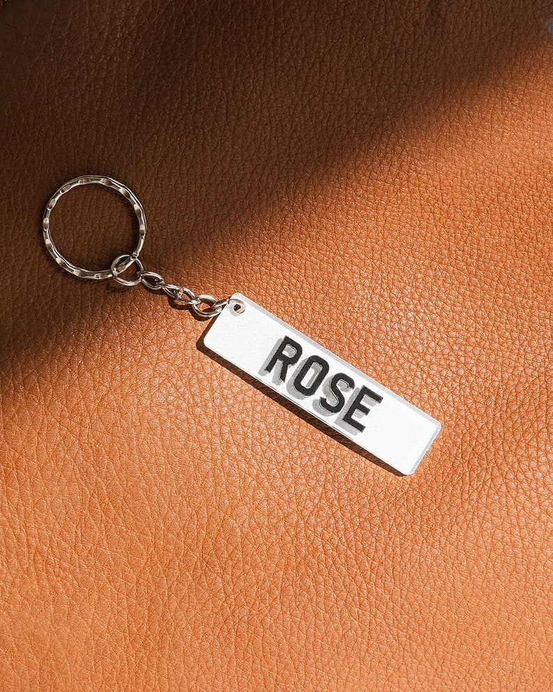 May include: A silver keychain with a white rectangular tag that says "ROSE" in black letters.