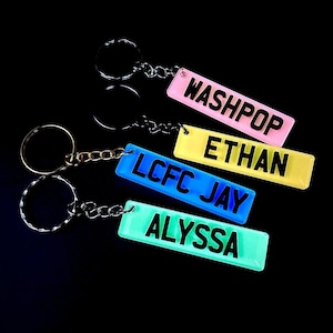 May include: Four colourful keychains with different names on them: Washpop, Ethan, LCFC Jay, and Alyssa. The keychains are made of plastic and have a shiny finish.