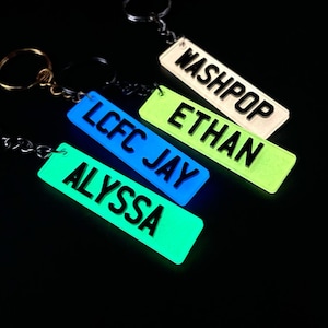 Op de afbeelding: Vier glow-in-the-dark sleutelhangers met verschillende namen: Washpop, Ethan, LCFC Jay en Alyssa. De sleutelhangers zijn allemaal in verschillende kleuren: wit, groen, blauw en groen.