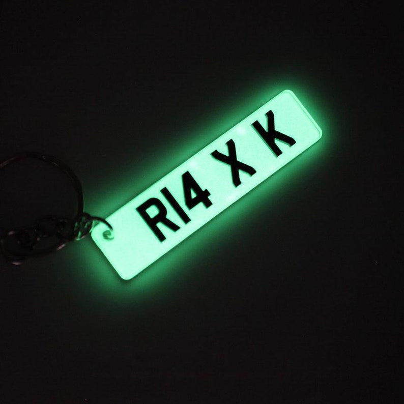 Op de afbeelding: Een glow-in-the-dark sleutelhanger met een zwart kentekenplaatontwerp met de tekst "R14 XK".
