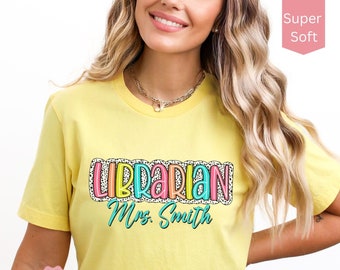 Op de afbeelding: Geel T-shirt met de tekst "Librarian Mrs. Smith" in kleurrijke letters met een wit stippenpatroon.