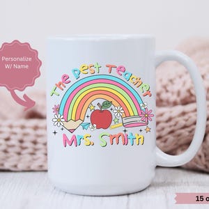 May include: White ceramic mug with a rainbow, apple, and pencil design. The text "The Best Teacher" and "Mrs. Smith" is printed on the mug. The mug is 15 ounces.