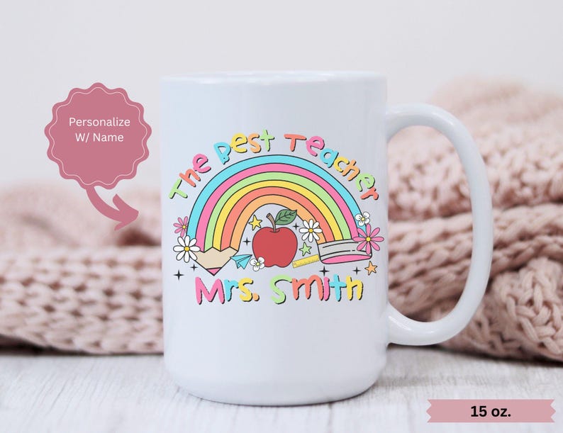 May include: White ceramic mug with a rainbow, apple, and pencil design. The text "The Best Teacher" and "Mrs. Smith" is printed on the mug. The mug is 15 ounces.