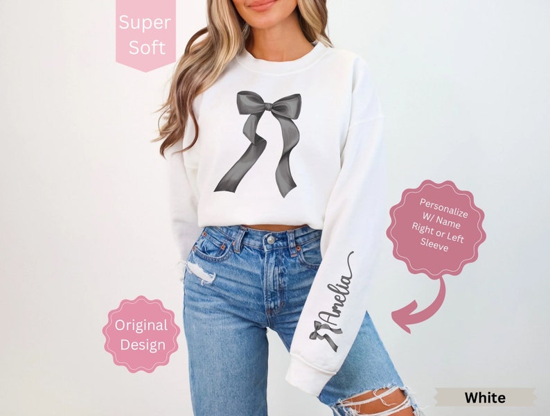 May include: White sweatshirt with a large gray bow graphic on the front. The sleeve features the name "Amelia" in a script font. The text "Super Soft", "Original Design", and "Personalize W/ Name Right or Left Sleeve" are also visible.
