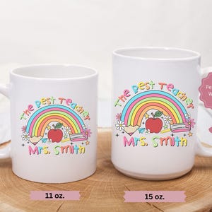 May include: Two white ceramic mugs with a rainbow, apple, and pencils design. The text on the mugs reads "The Best Teacher" and "Mrs. Smith". The mugs are available in 11 oz and 15 oz sizes.