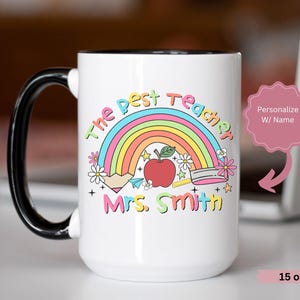 May include: White ceramic mug with a black handle. The mug has a rainbow, a red apple, and the text "The Best Teacher" and "Mrs. Smith". The mug is 15 oz.