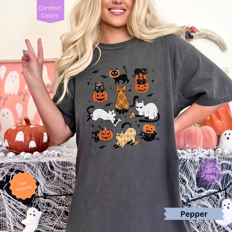 May include: A dark gray t-shirt with a graphic print of black and white cats with pumpkins and bats. The text "Pepper" is visible at the bottom of the image.