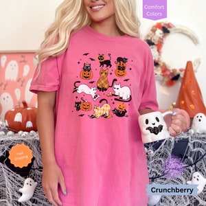 May include: Pink t-shirt with a graphic of black and white cats dressed up for Halloween with pumpkins and bats. The text "Crunchberry" is visible at the bottom of the image.