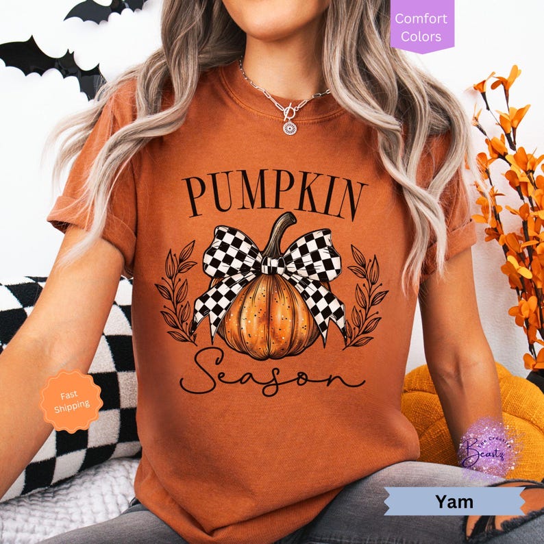 May include: A rust-colored t-shirt with a graphic of a pumpkin with a black and white checkered bow. The text "Pumpkin Season" is written below the pumpkin.