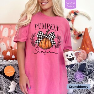 May include: A pink t-shirt with a black and white checkered bow on a pumpkin with the text "Pumpkin Season".