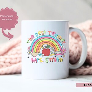 May include: White ceramic mug with a rainbow, apple, pencil, and ruler design. The text "The Best Teacher" and "Mrs. Smith" is printed on the mug. The mug is 11 ounces.