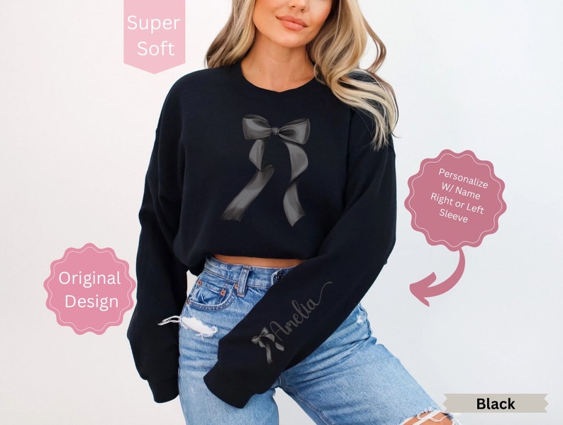 May include: Black sweatshirt featuring a gray bow design. The sleeve is personalized with a name in cursive. The text "Super Soft" and "Original Design" are also visible. The sweatshirt is black.