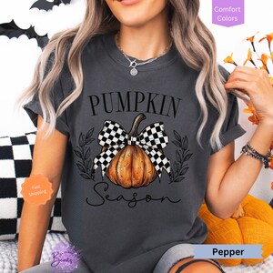 May include: A gray t-shirt with a black and white checkered bow on a pumpkin with the text "Pumpkin Season".